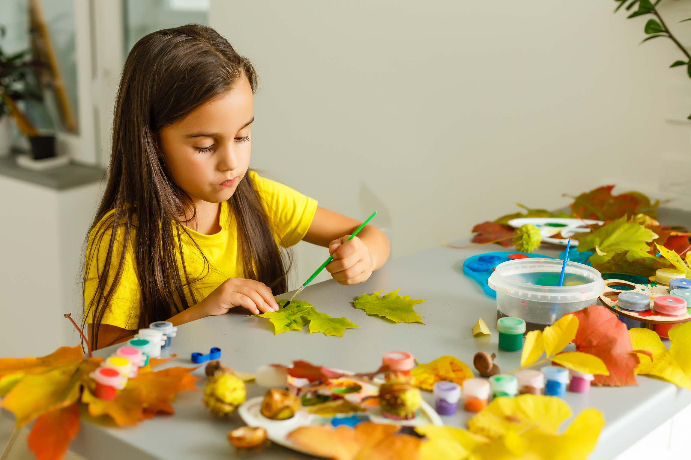 Little girl painting on autumn yellow leaves with gouache, kids arts, children creativity, autumn art.